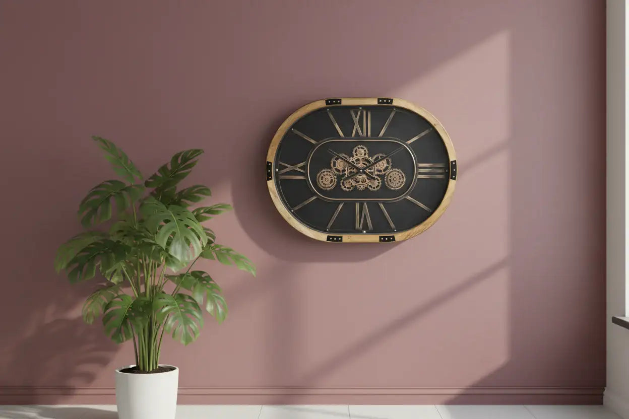 Decorative wall clock with gold frame and black face on a pink wall, next to a potted plant.