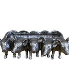 Set of five metal pig figurines on a wooden surface with a stone wall background