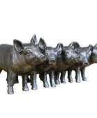 Set of five metallic pig figurines on a wooden surface with a stone wall background.