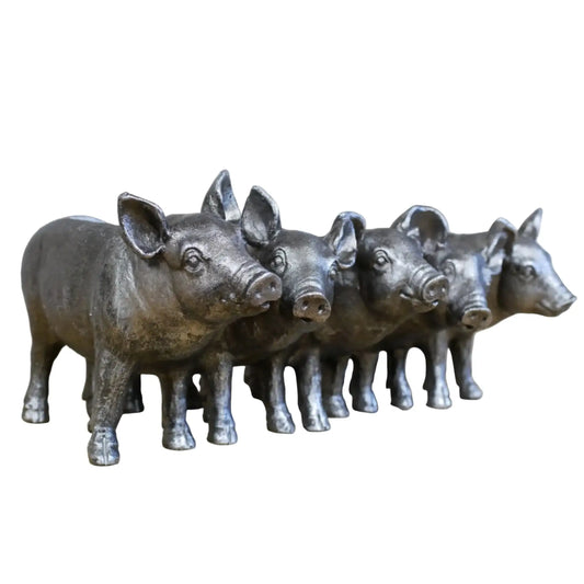 Set of five metallic pig figurines on a wooden surface with a stone wall background.