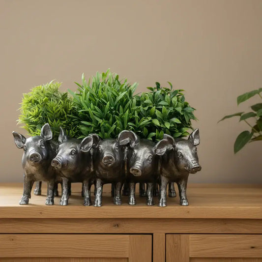 Five pig-shaped planters with green plants inside on a wooden surface.