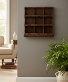 A dark brown wooden 9-compartment wall organizer with small metal clips, mounted on a gray wall in a styled living room setting with a potted fern and armchair visible.