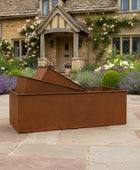 Rust-colored metal fire pit on a stone patio with a garden and house in the background