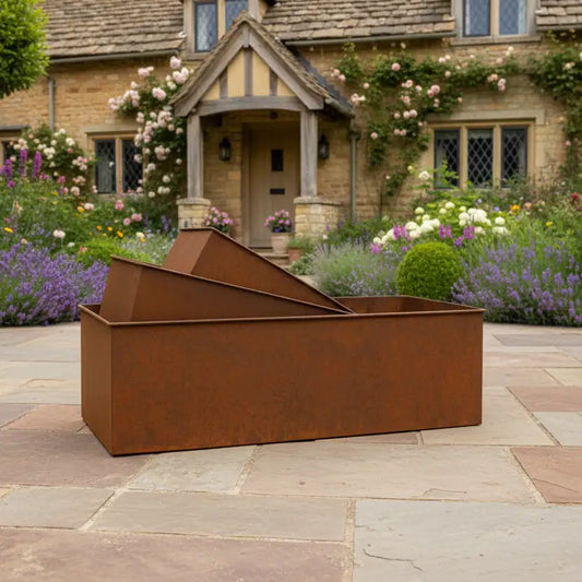 Rust-colored metal planter in a garden setting with a house in the background