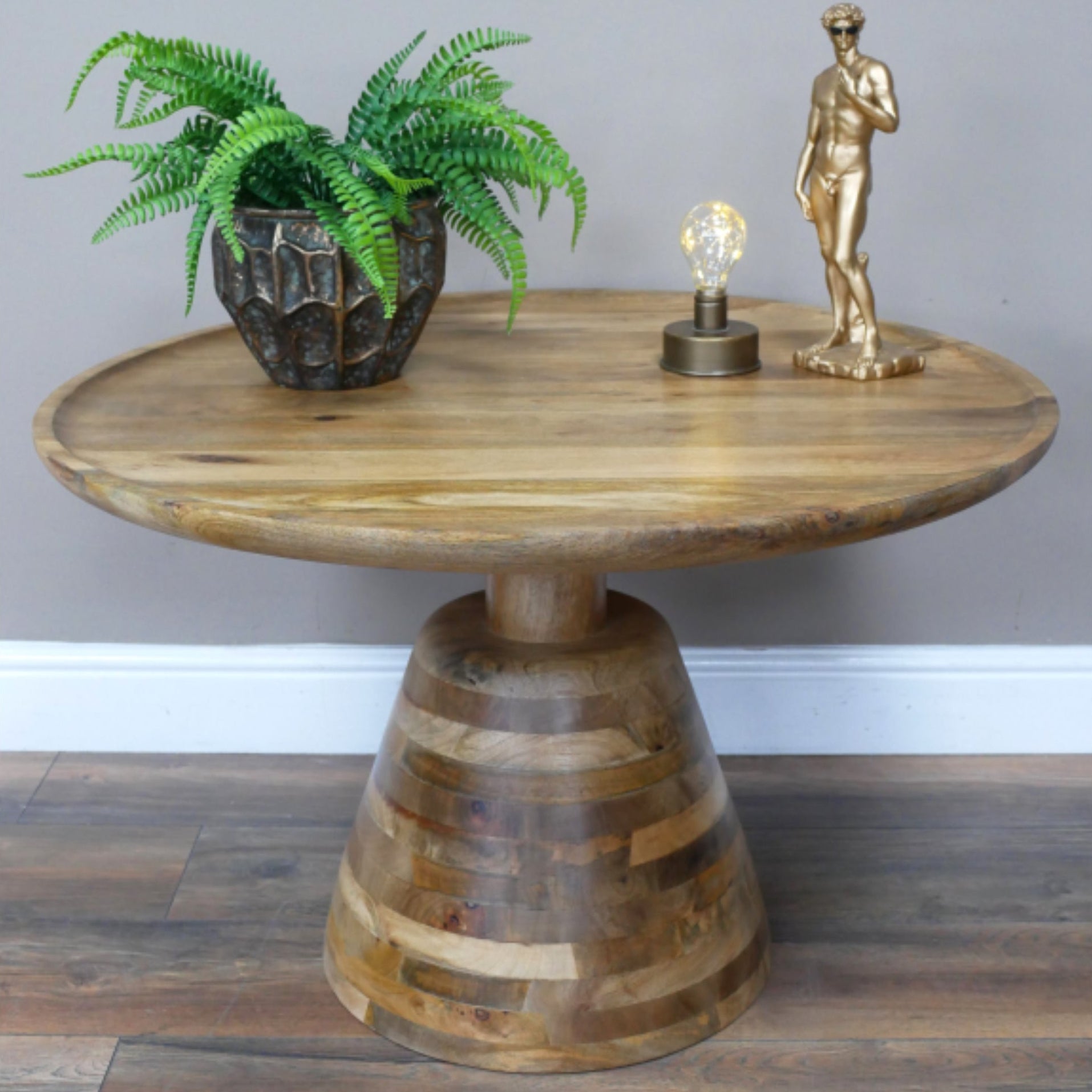 Wooden side table with a plant, lamp, and statue on a gray wall background