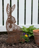 Metal rabbit sculpture in a garden setting with a white fence and potted plant.
