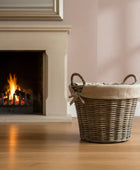 Wicker basket on a wooden floor in front of a fireplace with pink wall.