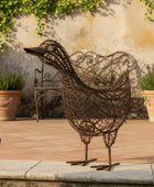 Decorative wire bird sculpture on a patio with potted plants and a bench.