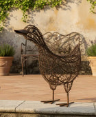 Decorative metal duck sculpture on a patio with potted plants and a stone wall in the background.