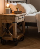 Wooden nightstand with lamp and books next to a bed in a bedroom setting