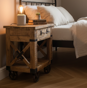 Wooden nightstand with lamp and books next to a bed in a bedroom setting