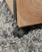 Wooden furniture leg with black caster wheel on a gray carpet
