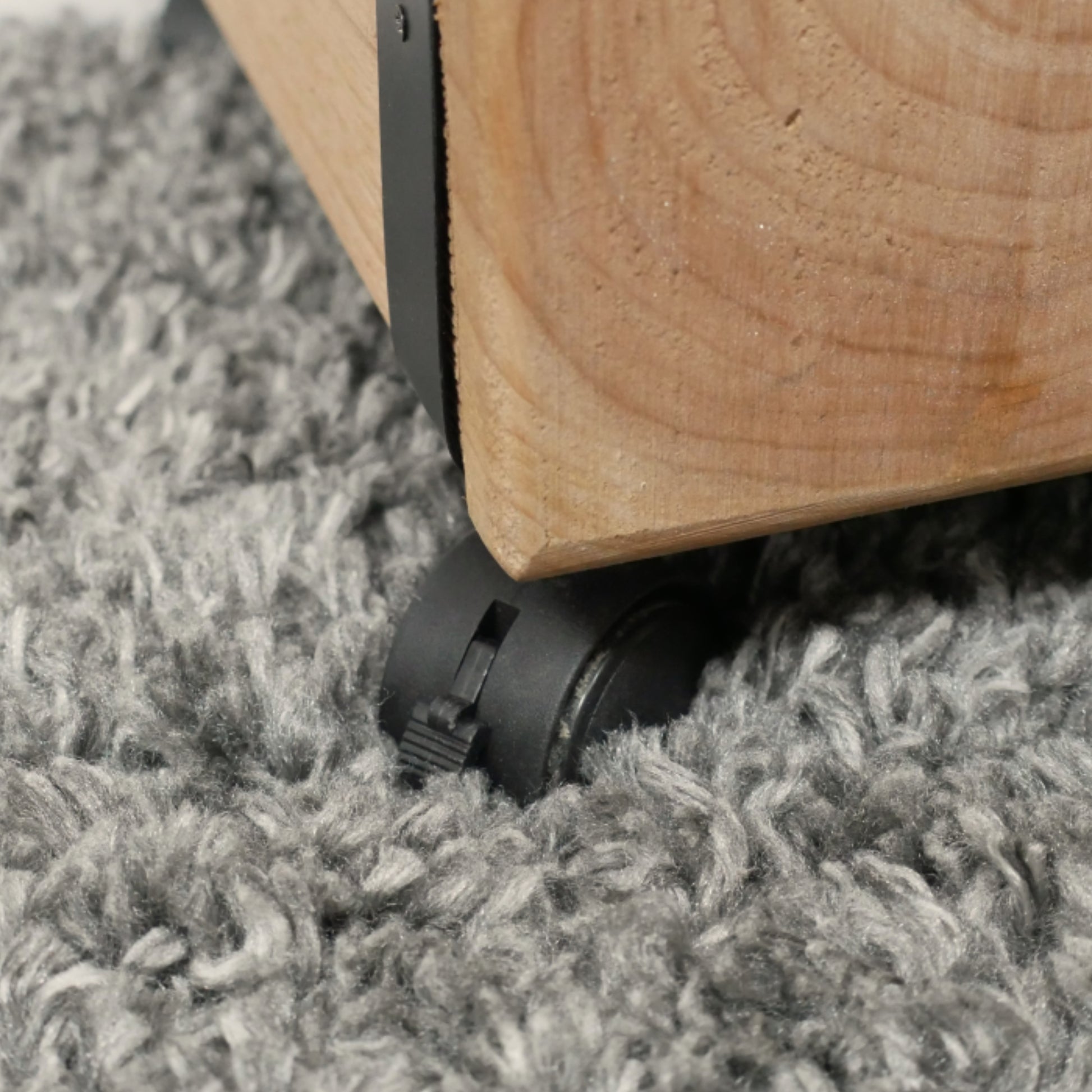 Wooden furniture leg with black caster wheel on a gray carpet