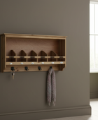 Wooden wall-mounted coat rack with hooks on a gray wall.