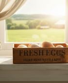 Wooden box of fresh eggs on a windowsill with a view of a farm outside.