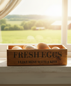 Wooden box of fresh eggs on a windowsill with a scenic view outside.