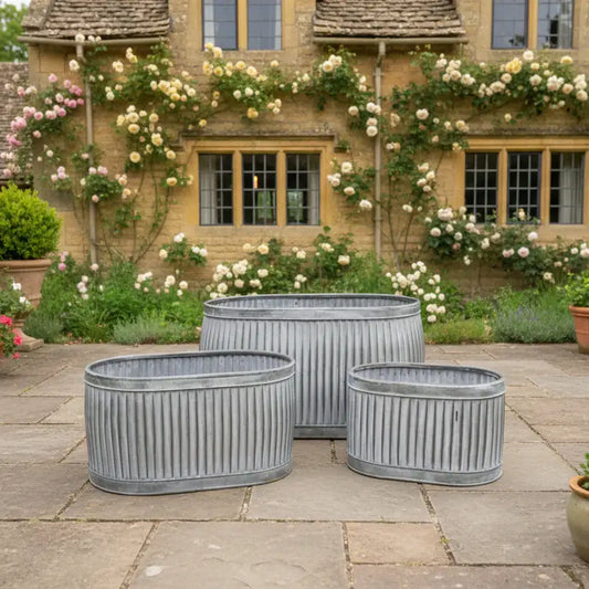 Decorative metal planters on a stone patio with a garden and house in the background