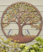 Decorative metal tree wall art on a wooden wall with plants in the foreground.
