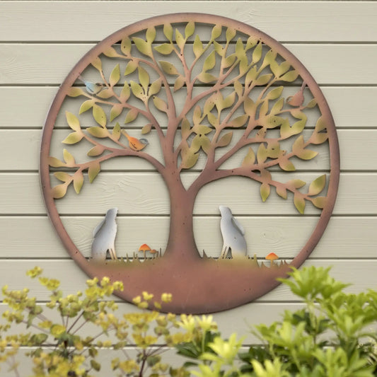 Decorative metal tree wall art on a wooden wall with plants in the foreground.