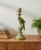 Decorative candlestick with bird figure on a wooden surface with books and a plant.