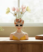 Vase shaped like a woman's head with sunglasses and flowers on a wooden surface