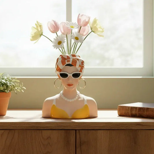 Vase shaped like a woman's head with sunglasses and flowers on a wooden surface