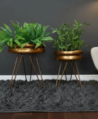 Two potted plants in bronze planters with metal stands on a gray carpet.
