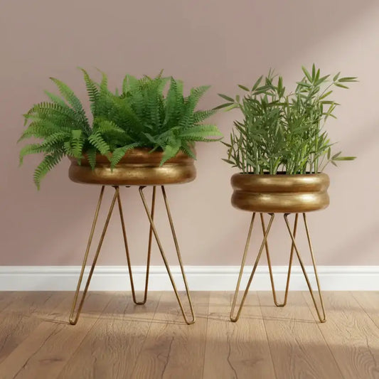 Two potted plants on gold stands against a pink wall.