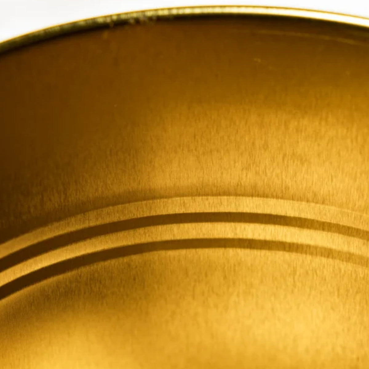 Close-up of a brushed metallic gold surface with concentric circular ridges and a thin reflective rim at the top.