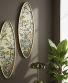 Two oval wall art pieces with nature-themed designs on a brown wall, next to a plant and small lamp.