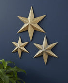 Three gold star-shaped wall decorations on a dark blue wall with a plant at the bottom left corner.