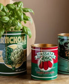 Recycled can planters with a basil plant, Passata can, and Olives can on a wooden surface.