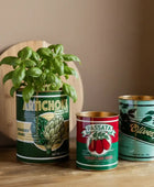 Three repurposed canned food planters with plants on a wooden surface.