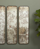 Three decorative wall mirrors with floral patterns on a green wall next to a plant.