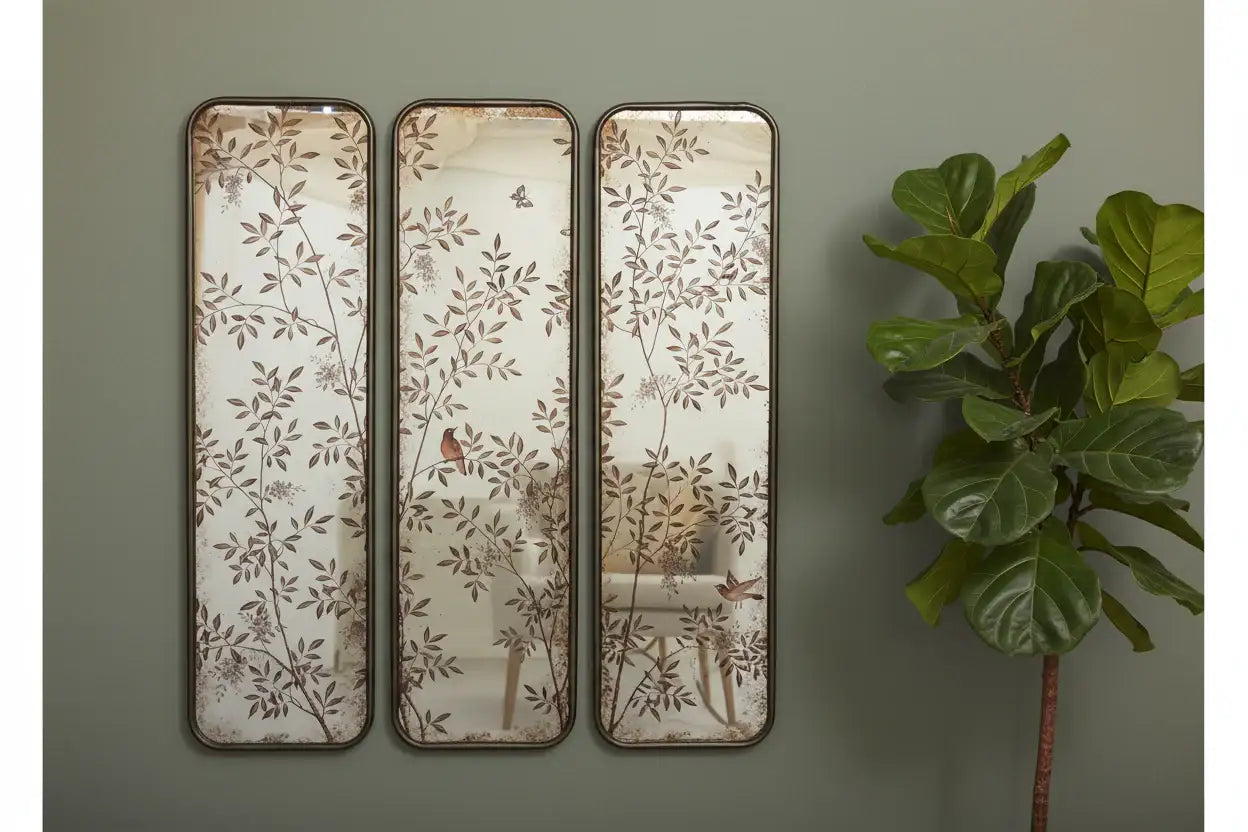Three decorative wall mirrors with floral patterns on a green wall next to a plant.