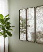Three decorative mirrors with leaf patterns on a wall next to a plant.