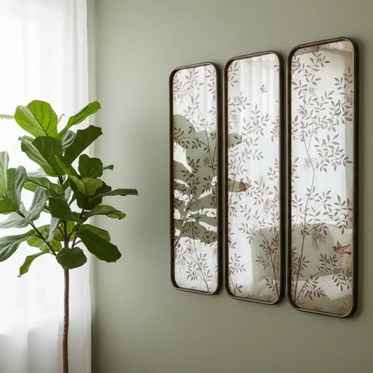 Three decorative mirrors with leaf patterns on a wall next to a plant.