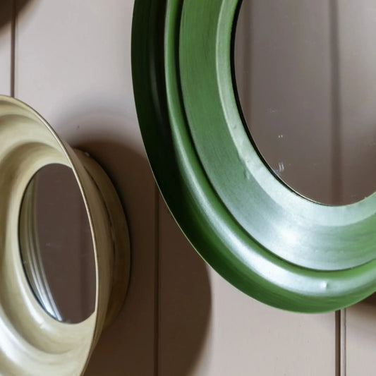 Two round mirrors, one green and one beige, on a wooden surface.