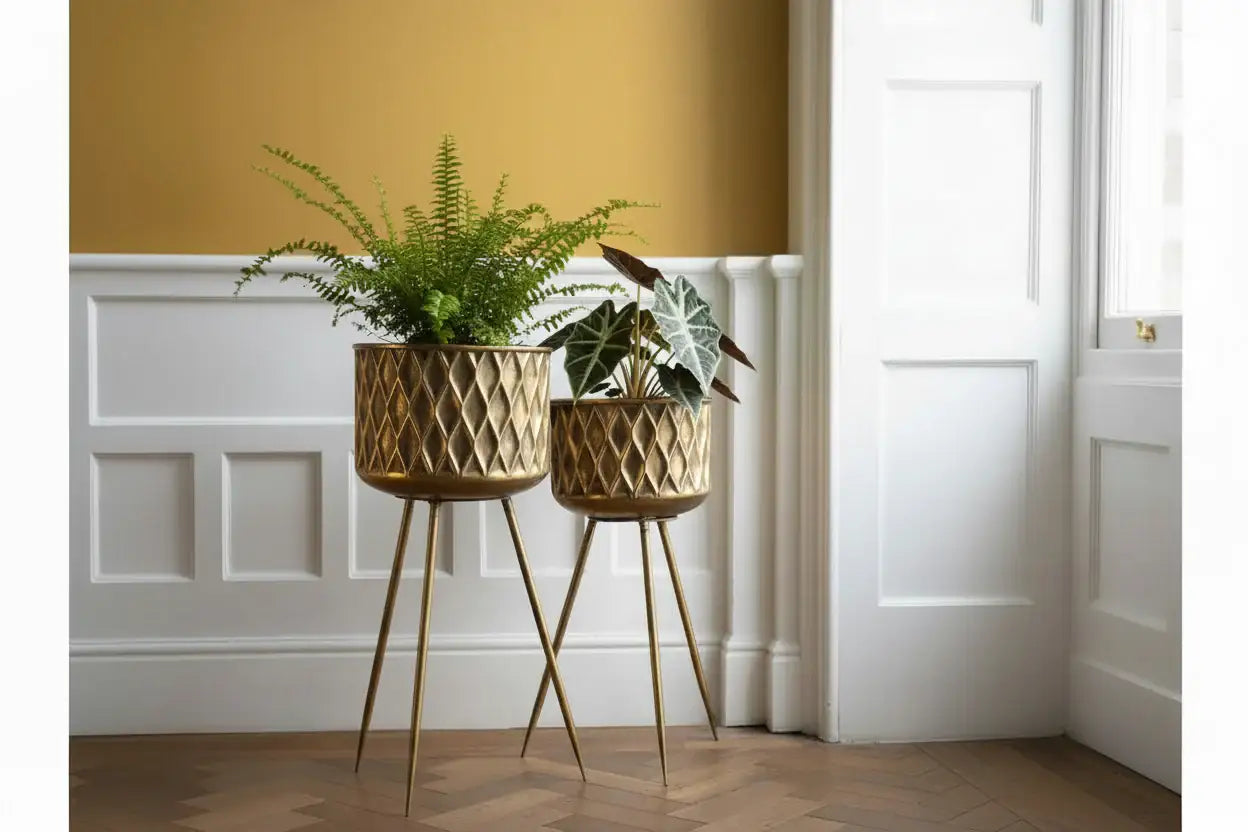Two gold geometric planters with plants on a wooden floor.