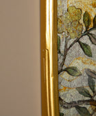 Close-up of a decorative mosaic tile wall featuring a floral pattern in muted green, gold, and gray tones, bordered by a prominent metallic gold frame on a wood surface.