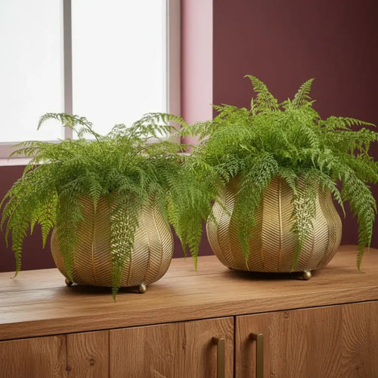 Gold leaf-patterned vases with green plants on a marble surface