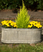 Metal planter with yellow flowers and a green shrub on a stone surface.
