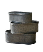 Three stacked metal planters on a gravel surface with a dark background