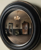 Round convex mirror with black frame reflecting indoor and outdoor elements.