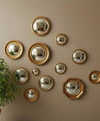 Gold wall mirrors of various sizes on a beige wall with a plant to the left.