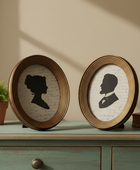 Two round wooden picture frames with silhouettes on a wooden surface with a plant and book in the background.