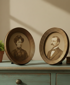Two framed portraits on a wooden shelf with a plant and book in the background.
