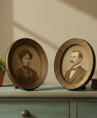 Two vintage-style oval frames with portraits of a man and a woman on a wooden surface.