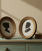 Two oval frames with silhouette portraits on a wooden surface.
