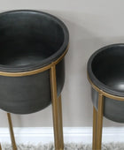 Two black planters with gold stands on a neutral background